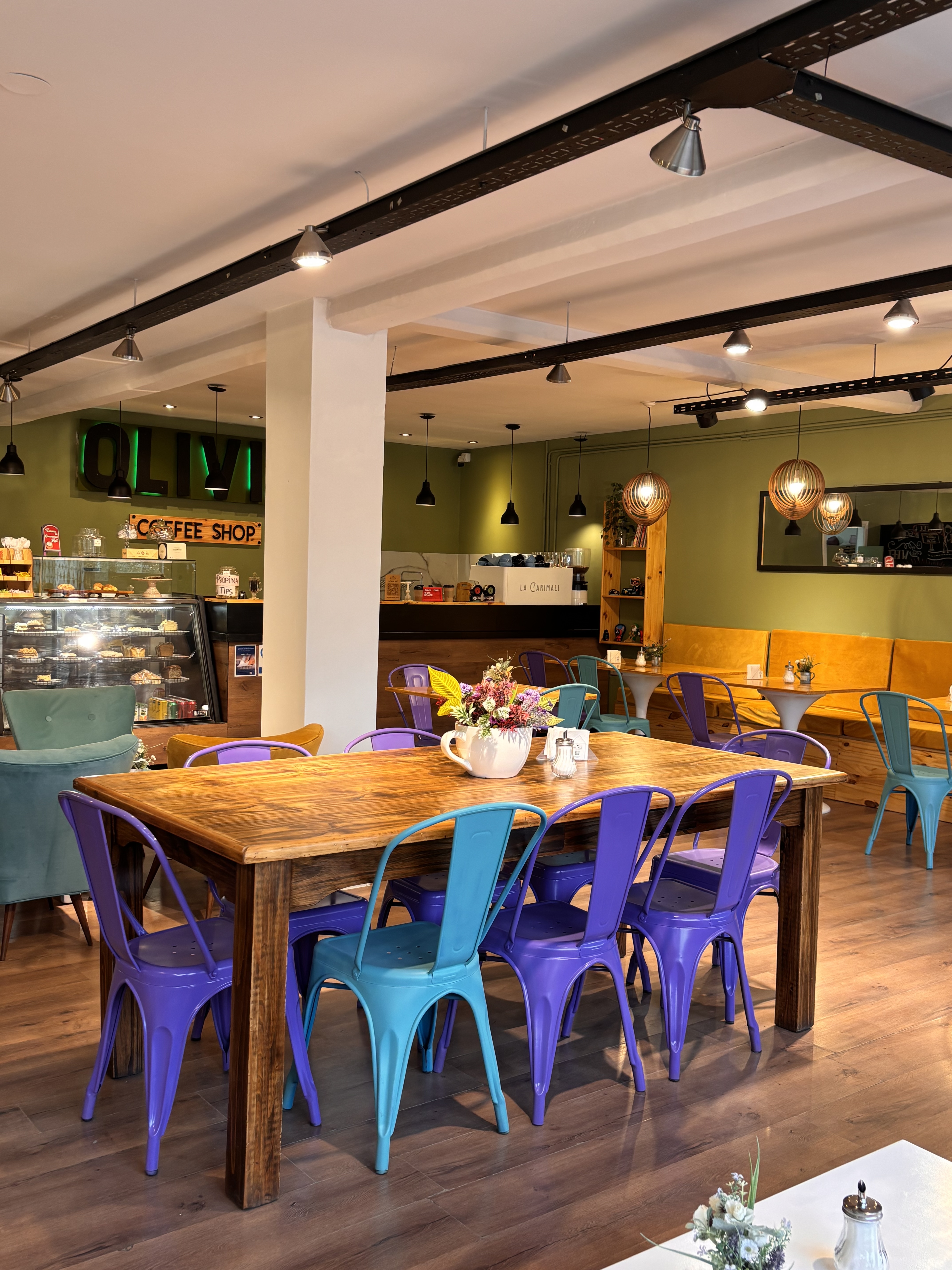Salón principal de Olivia Coffee Shop con mesa comunal y sillas de colores
